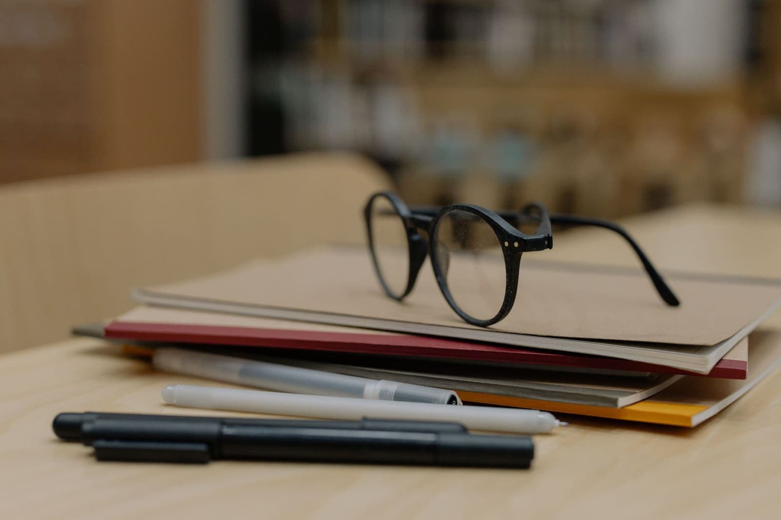 Een leesbril op een stapel notitieboeken met pennen op een houten tafel