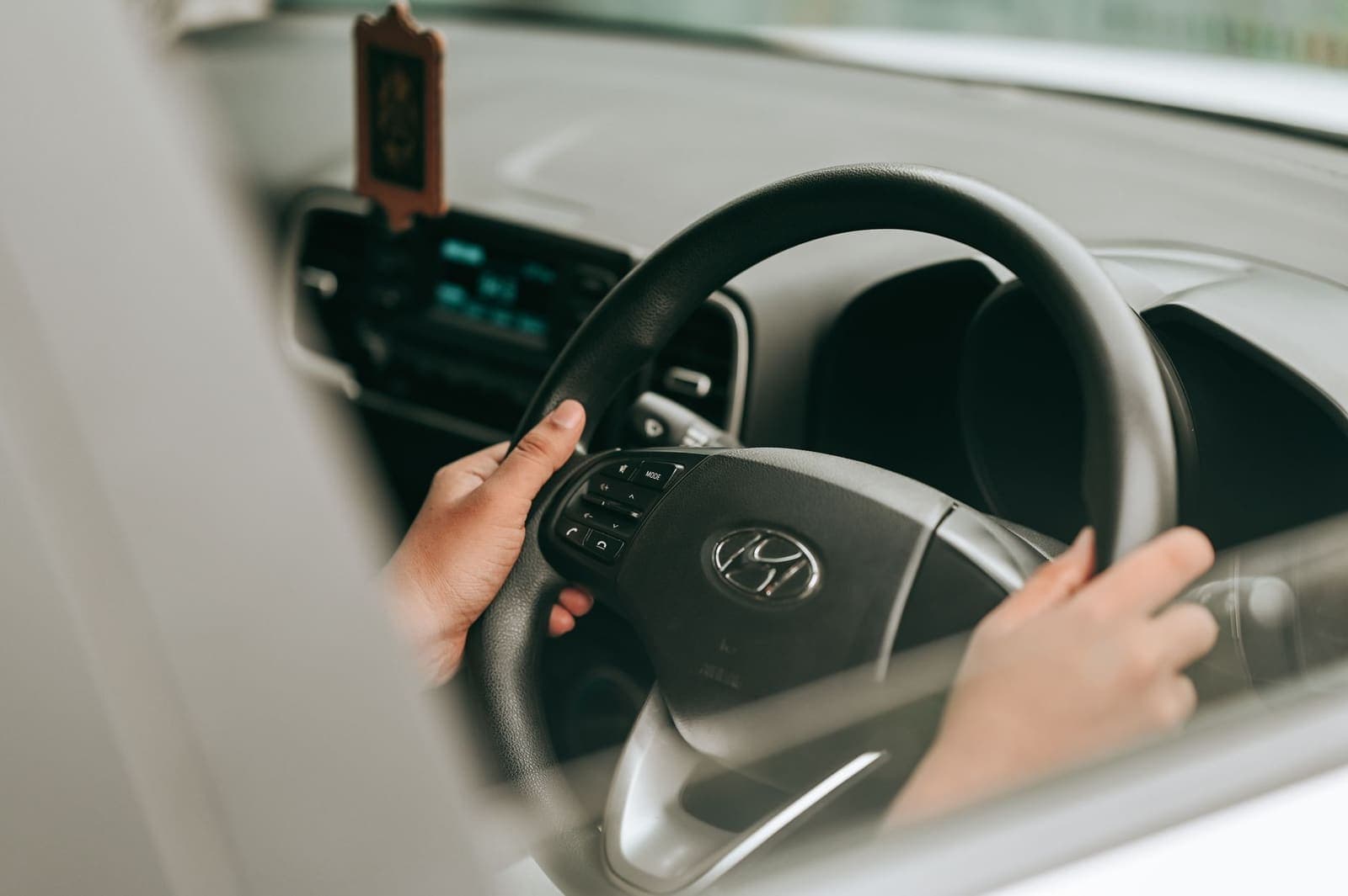 Twee handen aan het stuur van een rijdende auto, gezien door het zijraam