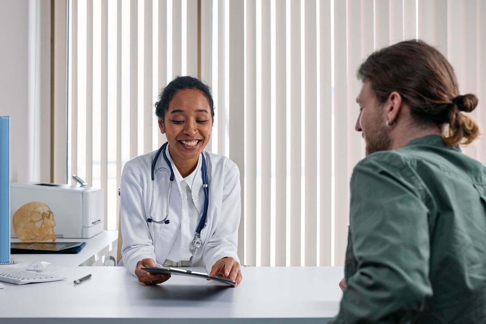 Een arts in gesprek met een patient aan een bureau in een lichte spreekkamer